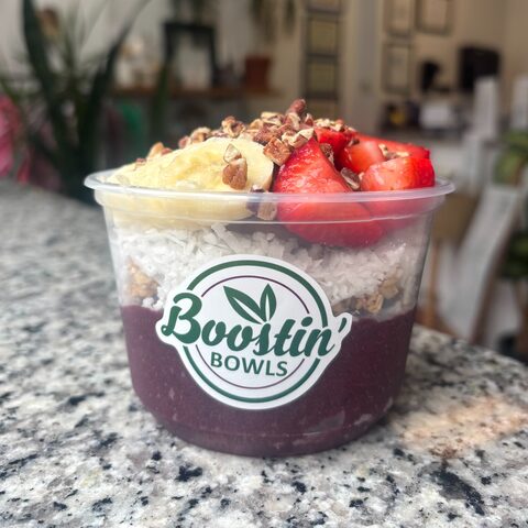 Purple bowl with granola, strawberries, banana, coconut, and pecans